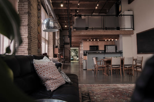 A spacious industrial loft with a black leather sofa, dining area, and mezzanine level